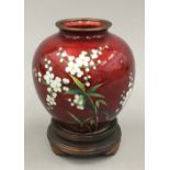 An Oriental ruby ground cloisonne vase decorated with white flowers on a wooden stand