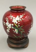 An Oriental ruby ground cloisonne vase decorated with white flowers on a wooden stand