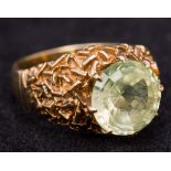 A contemporary 9 ct gold ring The pale green claw set stone above the bark effect shoulders.