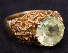 A contemporary 9 ct gold ring The pale green claw set stone above the bark effect shoulders.