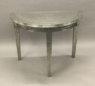 A decorative white metal covered demi-lune side table Set with beaten and polished metal sections.