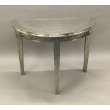 A decorative white metal covered demi-lune side table Set with beaten and polished metal sections.