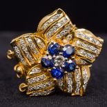 A diamond and sapphire set 14K gold clasp Of flowerhead form. 2.75 cm wide.
