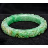 A Chinese carved apple green jade bangle Carved in the round with dragons. 8 cm diameter.