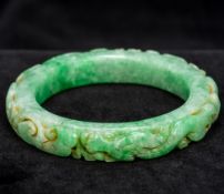 A Chinese carved apple green jade bangle Carved in the round with dragons. 8 cm diameter.