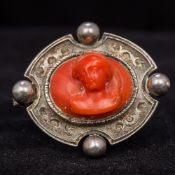 An antique unmarked white metal and carved coral brooch Centred with a classical bust. 4 cm wide.