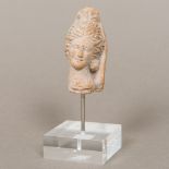 An antique terracotta fragment Worked as a female head wearing a headdress, on perspex plinth base.
