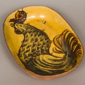 A slip decorated pottery dish Of rounded rectangular form, worked with a cockerel. 42.5 cm wide.