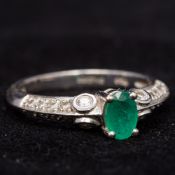 An 18 ct white gold diamond and emerald ring The central claw set emerald flanked by diamond set