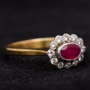 An 18 ct gold, diamond and ruby ring The central facet cut oval ruby bordered by a row of diamonds.