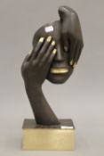 A contemporary bronze sculpture formed as two hands holding a face