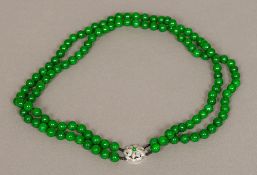 A 14K white gold diamond set jade bead necklace The twin strings with flowerhead clasp.