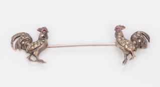 An unmarked white metal, polished steel and ruby set double pin Each end formed as a cockerel,