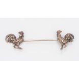 An unmarked white metal, polished steel and ruby set double pin Each end formed as a cockerel,