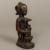 An African tribal carved wooden figurine Modelled as a female figure pounding a pestle and mortar.