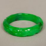 A Chinese apple green jade bangle Carved in the round with dragons. 7.5 cm diameter.