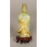 A Chinese carved jade figurine modelled as Guanyin Mounted on a carved wooden base. 27.5 cm high.