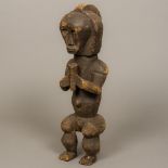 An African carved wooden tribal figure Of stylised human form, modelled seated wearing a headdress,