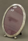 A large sterling silver oval photo frame with foliate engraved border on ball feet.