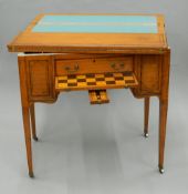 A Victorian inlaid satinwood games table The hinged revolving rectangular top enclosing a baize