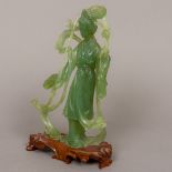 A Chinese translucent green hardstone figural carving Formed as Guanyin holding a flower to one