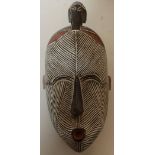 Unusual carved wood face mask with white and red highlighted detail, crested with carved figure of a