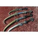 Four Arab type daggers with curved blades and brass & white metal sheathes with wooden grips, of