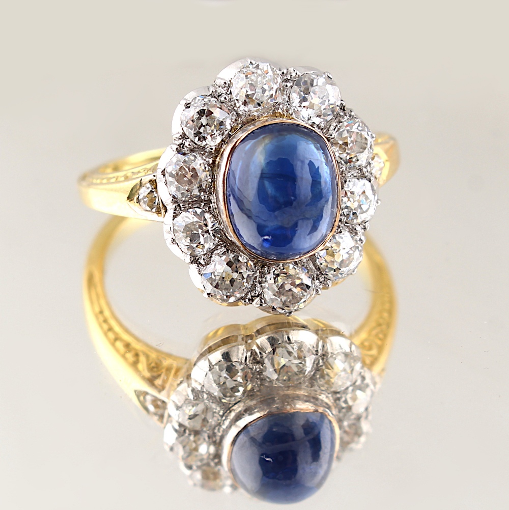 A yellow gold cabochon sapphire & diamond cluster ring, the oval cabochon sapphire weighing