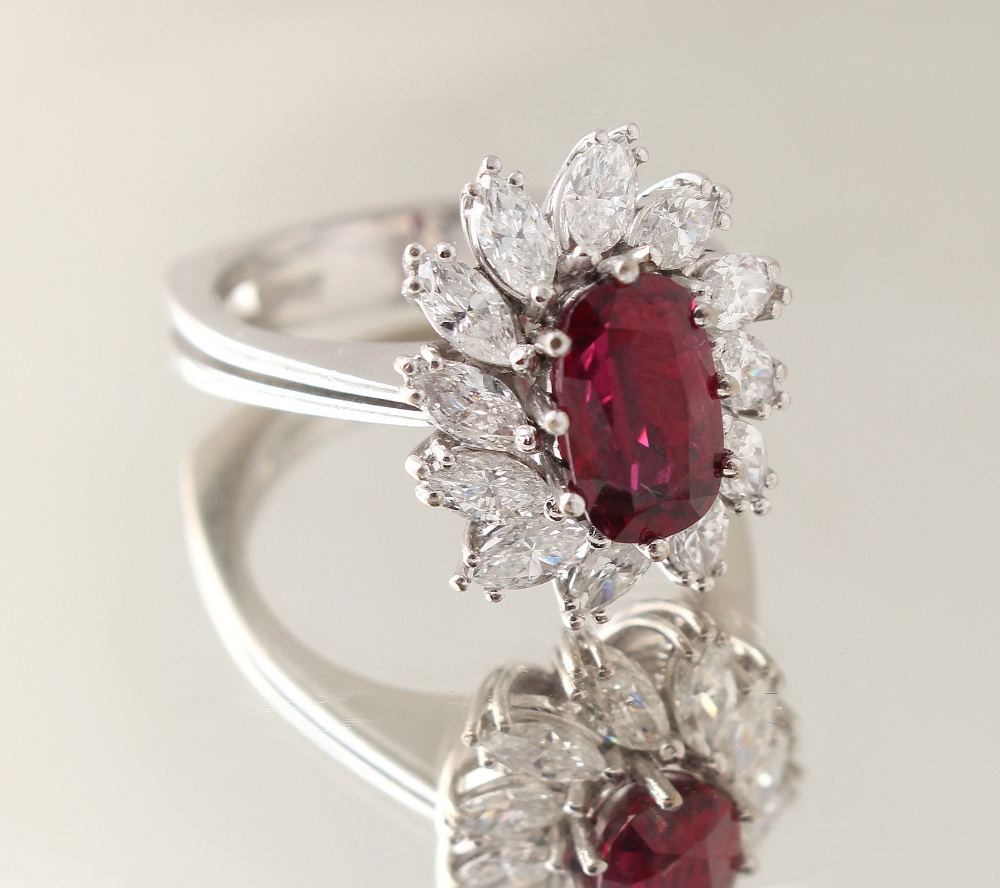 An 18ct white gold ruby & diamond floral cluster ring, the oval cushion cut ruby weighing