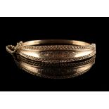 Property of a lady - a 9ct gold hinged bangle, with engraved foliate decoration & pierced borders,