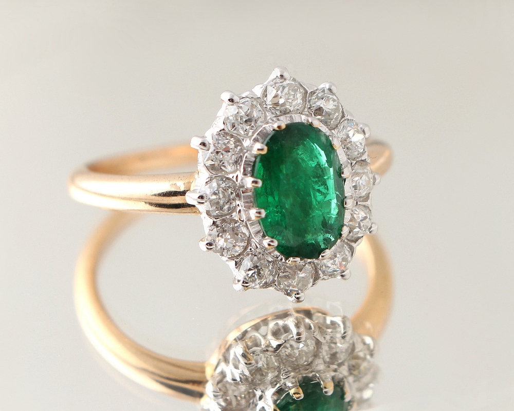 An unmarked yellow gold emerald & diamond cluster ring, the oval cut emerald approximately 0.80