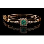A late Victorian unmarked yellow gold emerald & diamond hinged bangle, the certificated octagonal