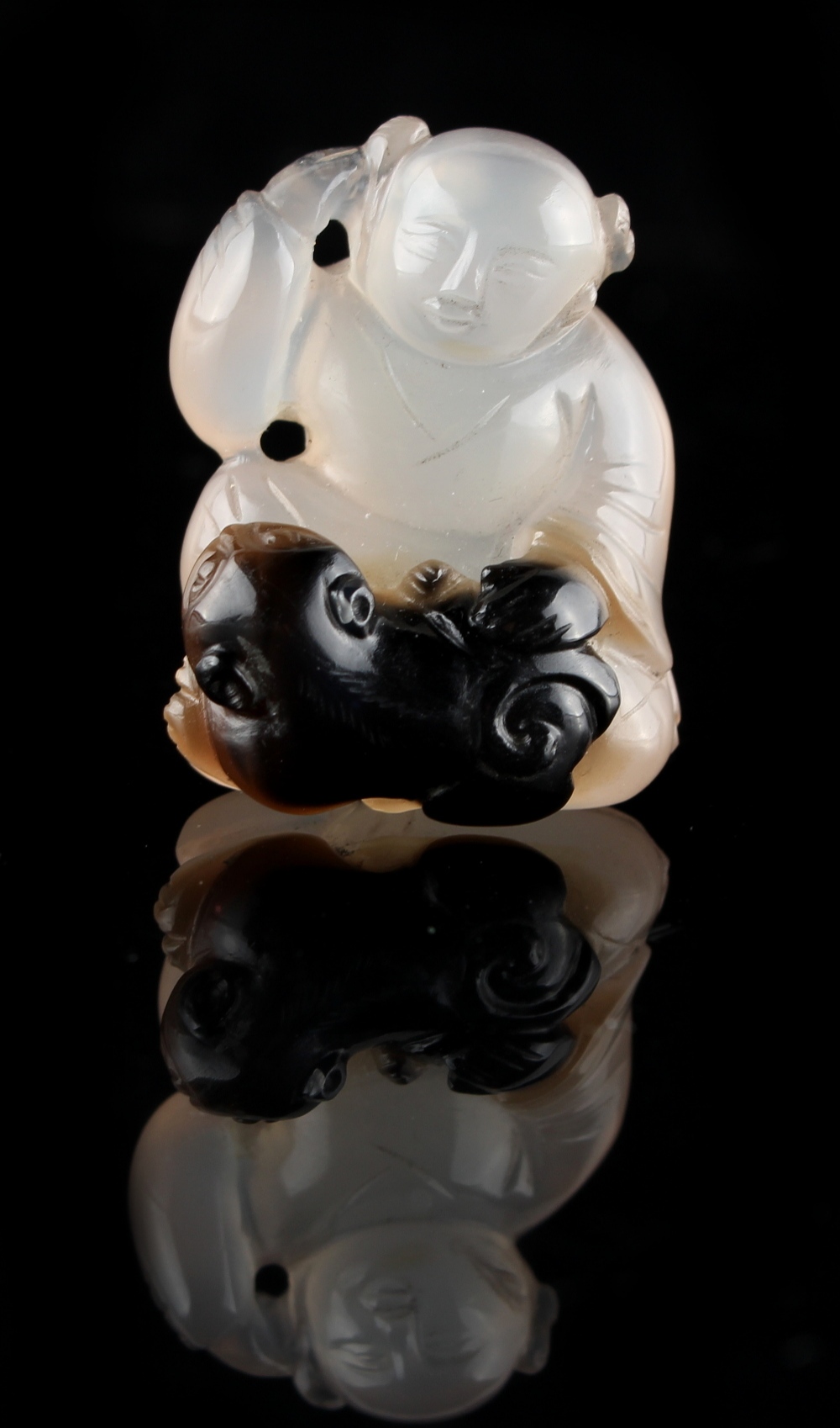 A Chinese carved agate figure of a seated boy with a cub at his feet, 1.35ins. (3.4cms.) high (see