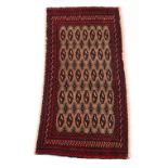 A Turkoman woollen hand-made rug with dark red ground, 50 by 24ins. (127 by 61cms.)