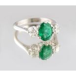 An unmarked platinum or white gold emerald & diamond three stone ring, the oval cut emerald weighing