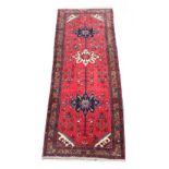 A Hamadan woollen hand-made carpet with red ground, 118 by 50ins. (300 by 125cms.).