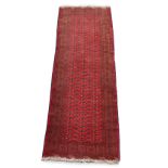 A Turkoman woollen hand-made carpet with red ground, 115 by 46ins. (290 by 103cms.).