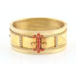 An unmarked Victorian yellow gold (tests 18ct) hinged bangle with buckle decoration set with coral &