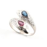 An unmarked white gold ruby sapphire & diamond twin snake head ring, the pear shaped cut ruby &