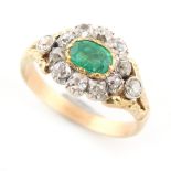 An unmarked yellow gold emerald & diamond cluster ring, the oval cut emerald weighing