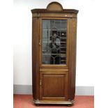 An Early XX Century Oak Double Corner Cupboard, with arched pediment, leaded glazed door over a