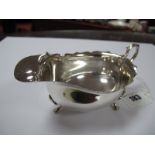 A Hallmarked Silver Sauce Boat, with wavy cut edge and scroll handle, raised on three shell capped