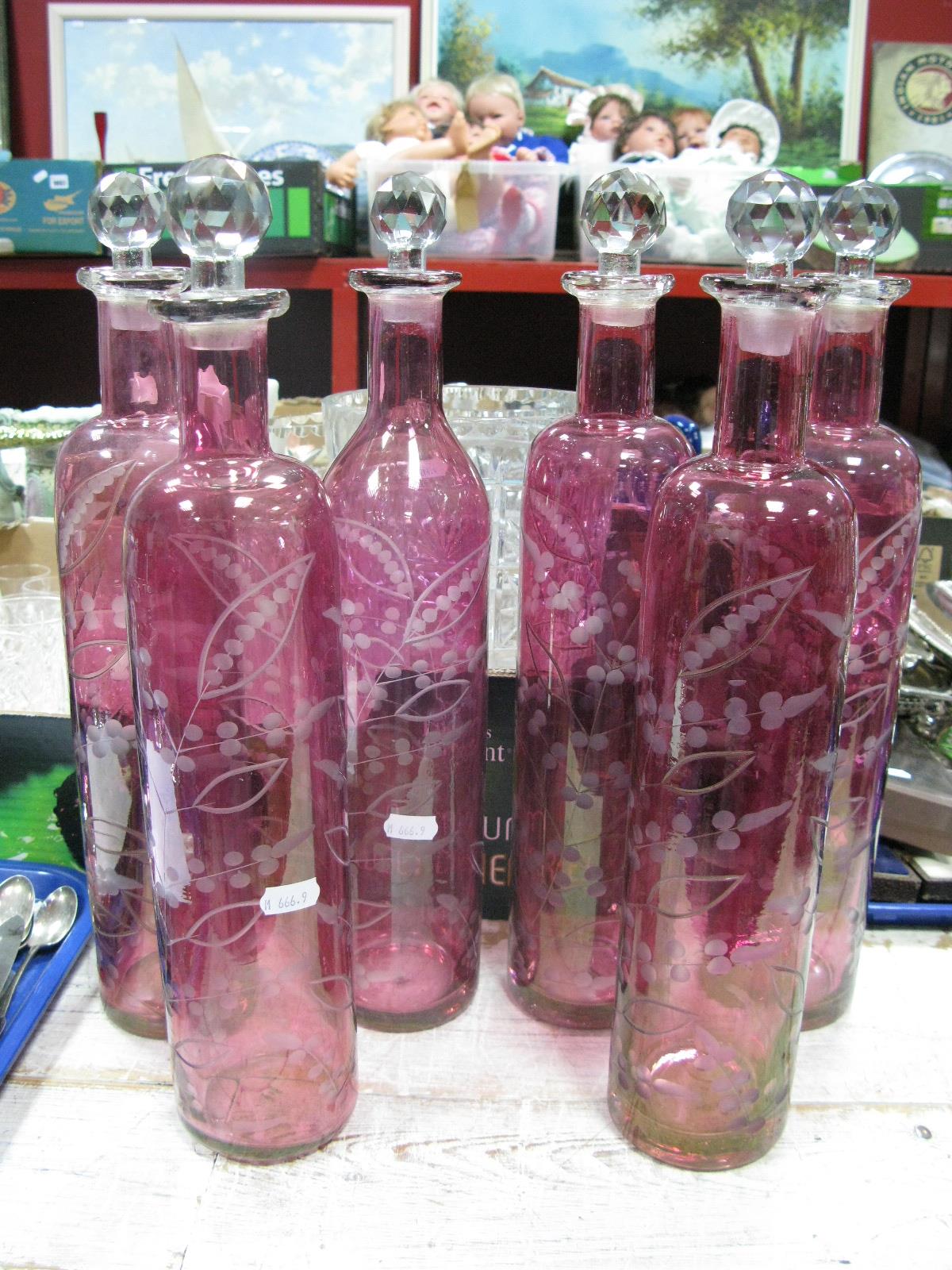 A Set of Six Cranberry Glass Cylindrical Bottles, engraved with foliage, faceted clear glass