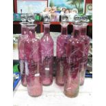 A Set of Six Cranberry Glass Cylindrical Bottles, engraved with foliage, faceted clear glass