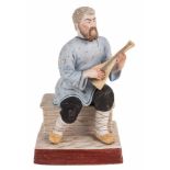 A RUSSIAN PORCELAIN FIGURE OF A SEATED BALALAIKA PLAYER, GARDNER PORCELAIN FACTORY LATE 19TH CENTURY