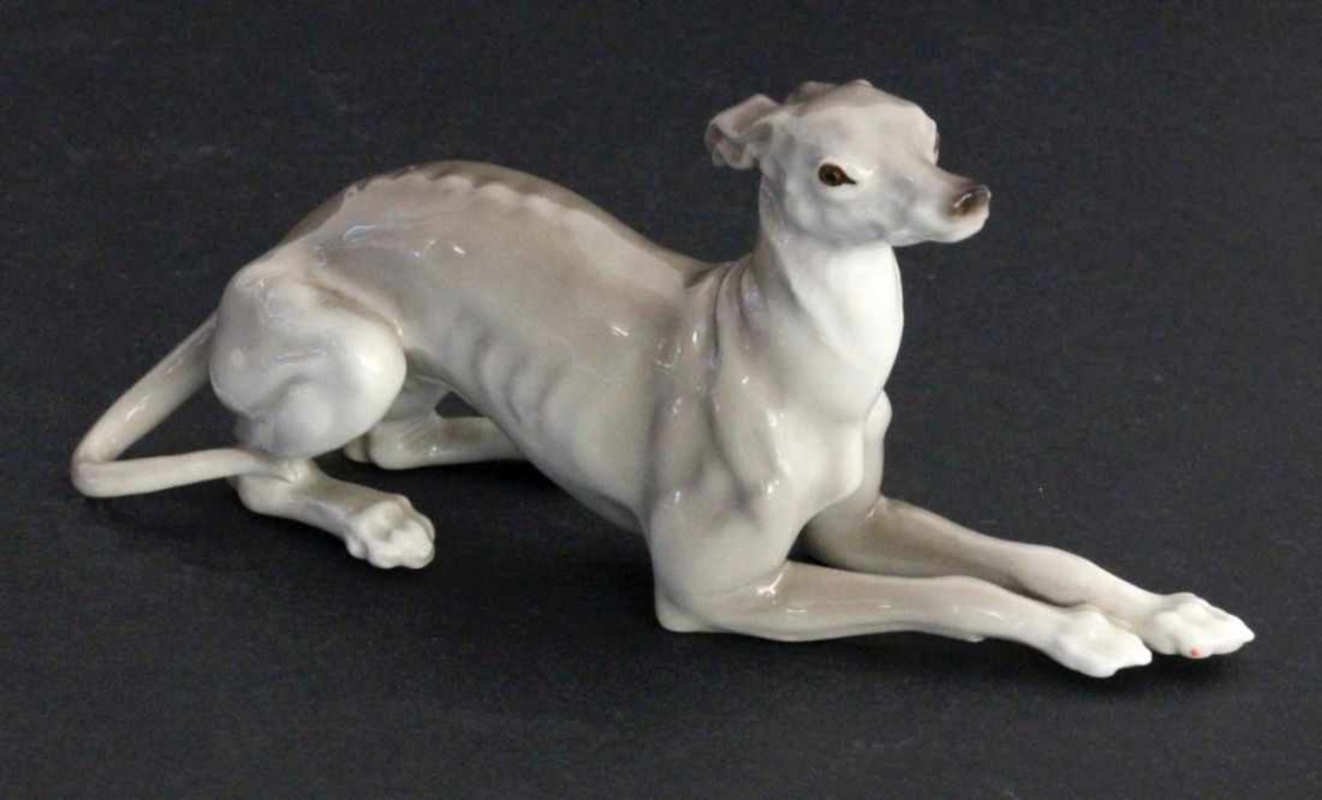 A LYING BORZOI Nymphenburg, 20th century Naturalistically decorated miniature sculpture.Model number