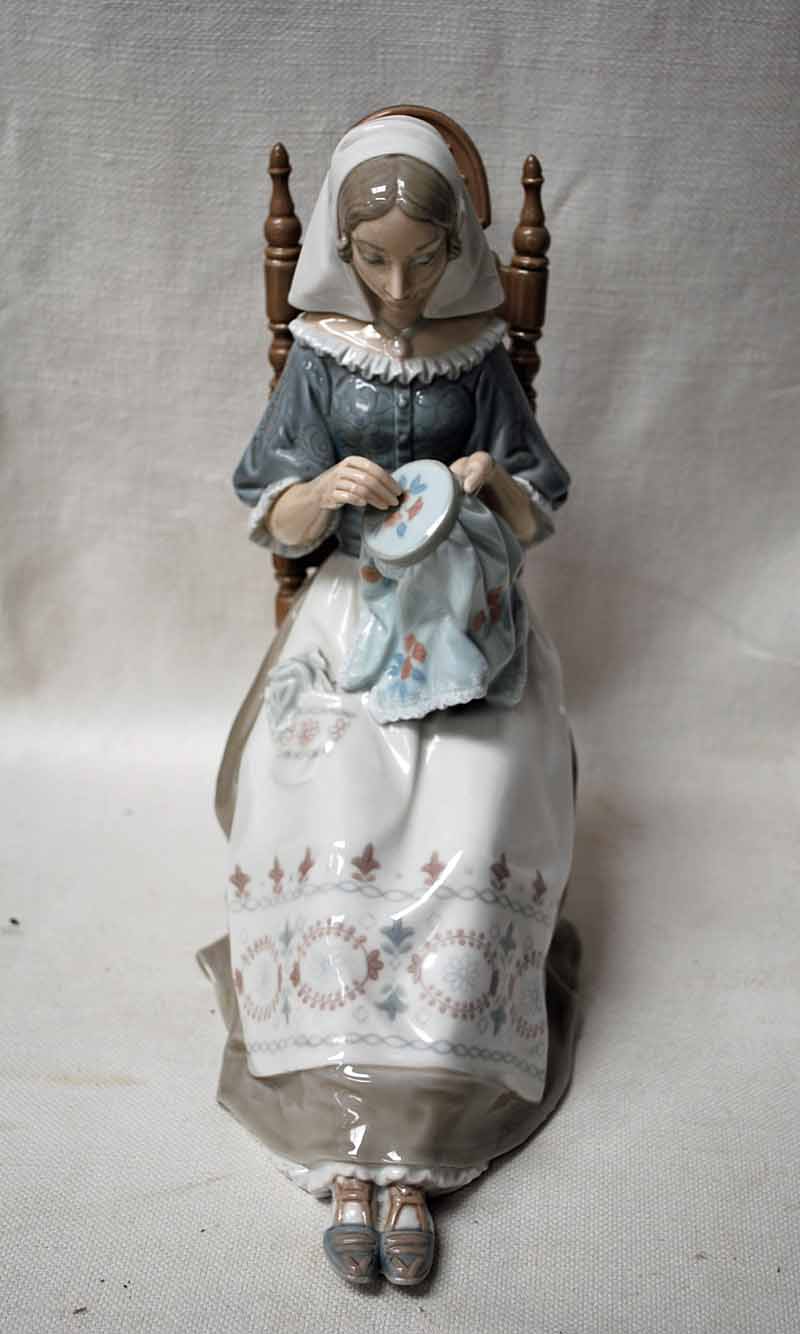 A large Lladro Figure as a young woman seated on a ladderback chair embroidering, 28cm high