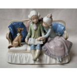 A Lladro Figural Group as a Boy and Girl seated on a Sofa reading with a Dog looking on, 26cm long