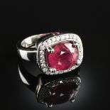A 14K WHITE GOLD, RUBY, AND DIAMOND HALO LADY'S RING, the mounting centering an oval cut ruby