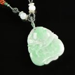 A NATURAL CARVED JADE PENDANT NECKLACE, the jade stone of pale green with white hues carved with